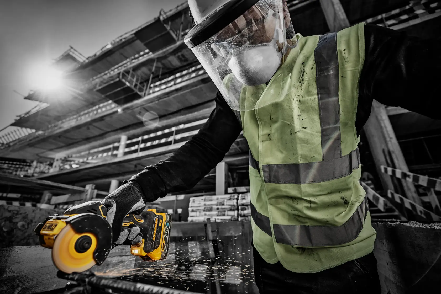 Una persona con pantalla protectora facial y chaleco de alta visibilidad utiliza una amoladora angular inalámbrica DEWALT para cortar metal, generando chispas, en un sitio de construcción.