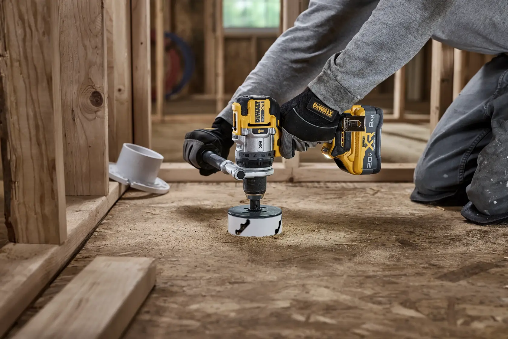 Persona usa un taladro inalámbrico DEWALT para cortar un agujero en un piso de madera en construcción.