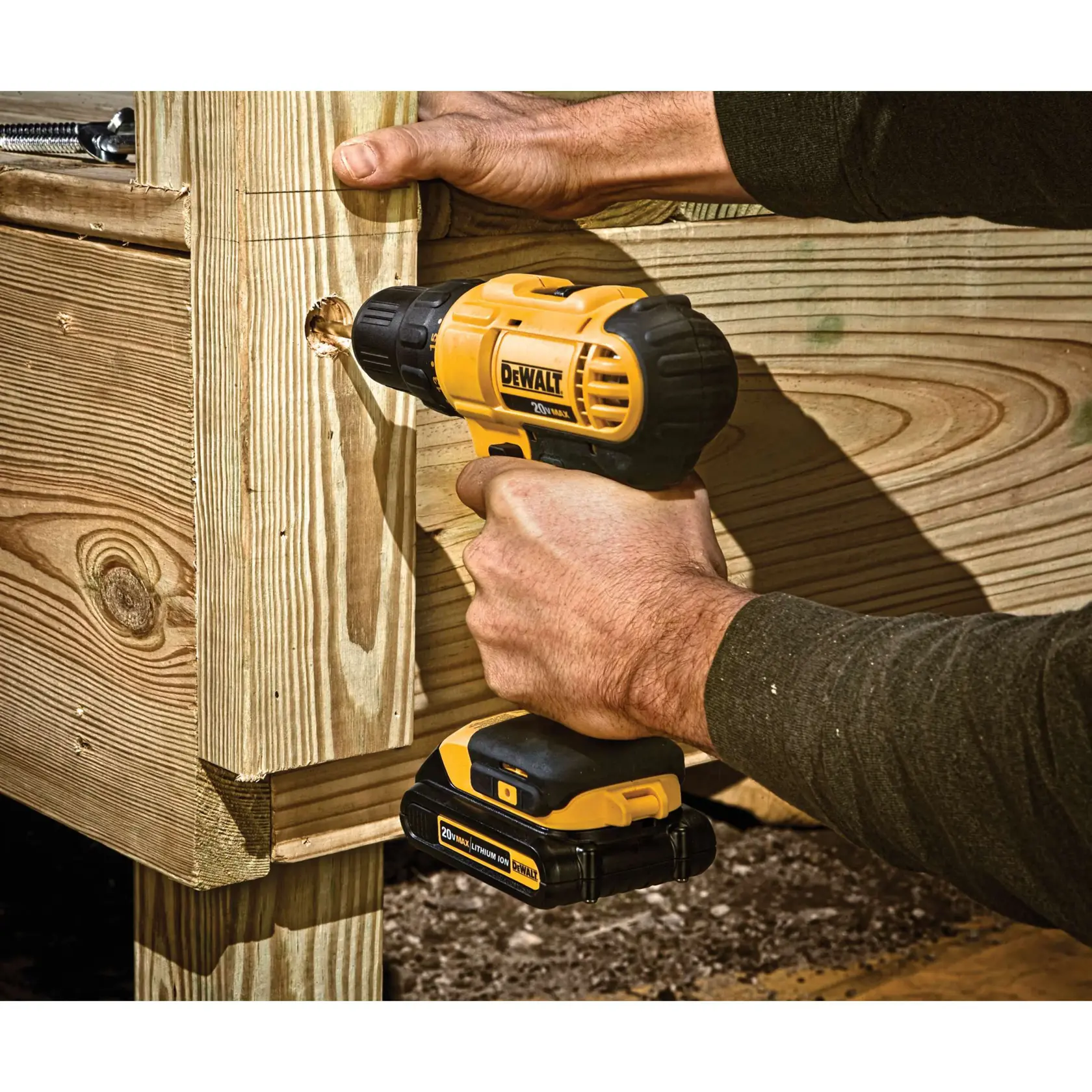 Una persona está usando un taladro inalámbrico amarillo y negro DEWALT para hacer un agujero en una estructura de madera.