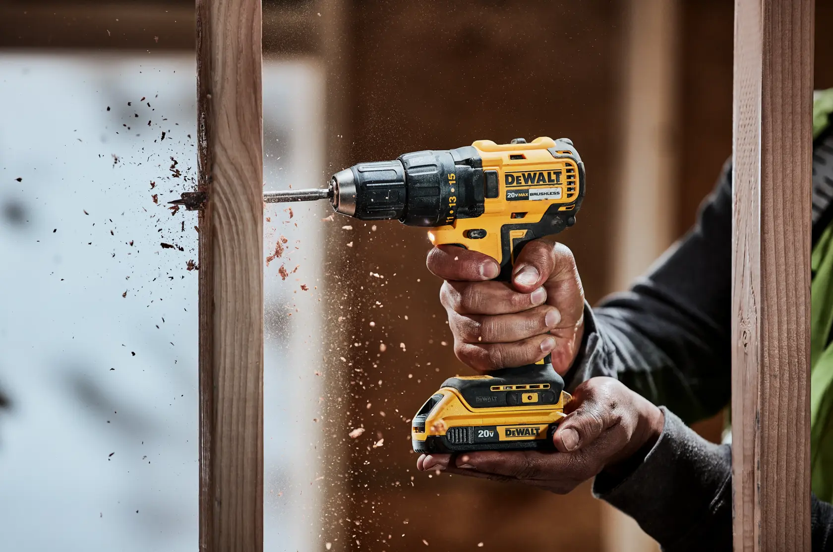 Primer plano de una persona usando un taladro inalámbrico amarillo y negro DEWALT para perforar una viga de madera, con virutas de madera saliendo del agujero.