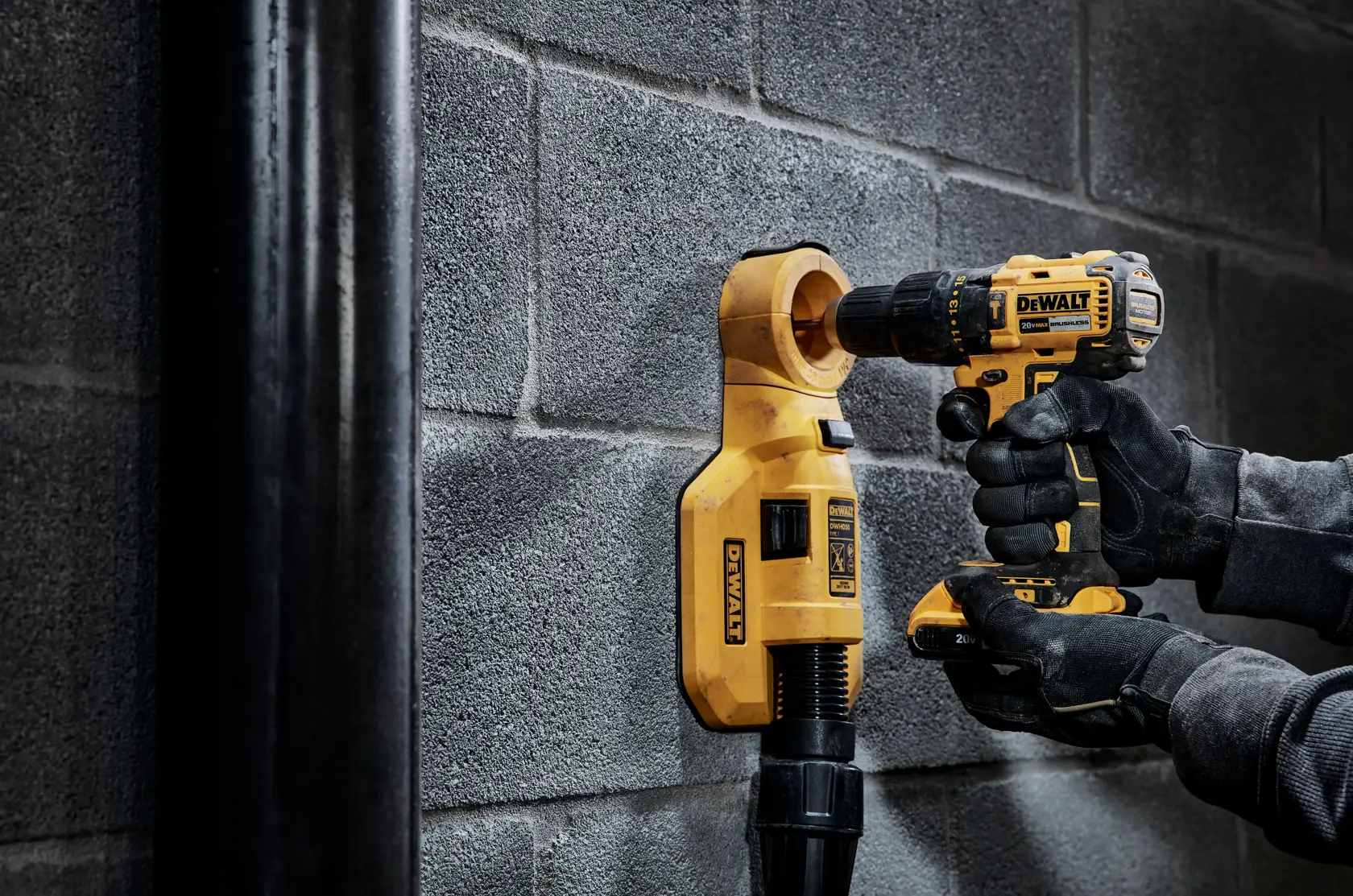 Una persona con guantes utiliza un taladro inalámbrico amarillo DEWALT para perforar una pared de hormigón, con un accesorio de extracción de polvo DEWALT para recolectar el polvo.