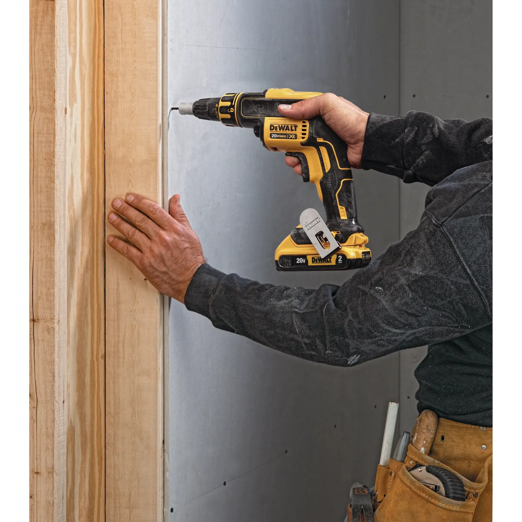 Una persona usa un destornillador inalámbrico DEWALT para fijar paneles de yeso a una viga de madera. La herramienta es amarilla y negra, y el usuario lleva un cinturón de trabajo con herramientas.