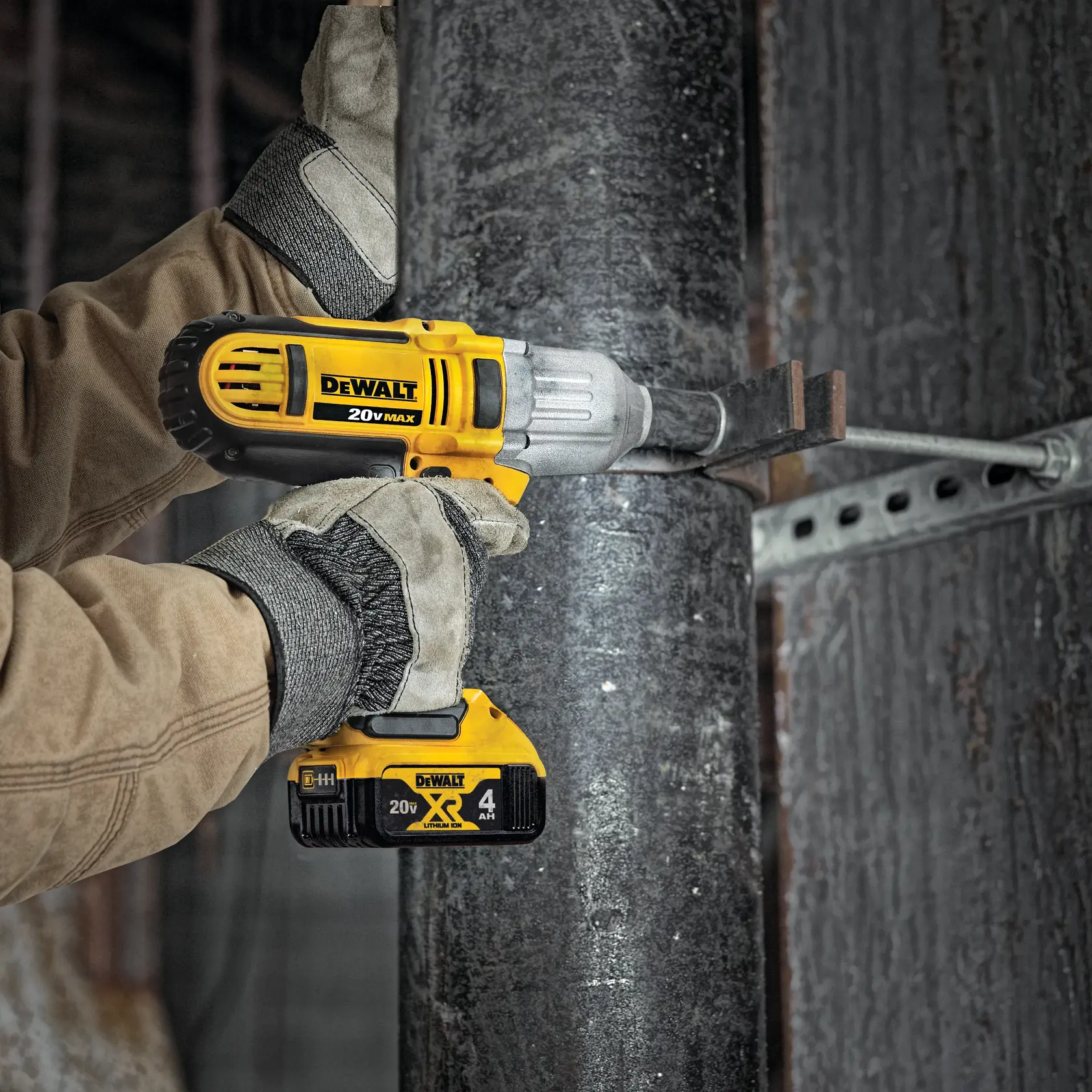Una persona con guantes de trabajo y chaqueta marrón utiliza una llave de impacto inalámbrica DEWALT 20V MAX para apretar un perno en una estructura metálica.