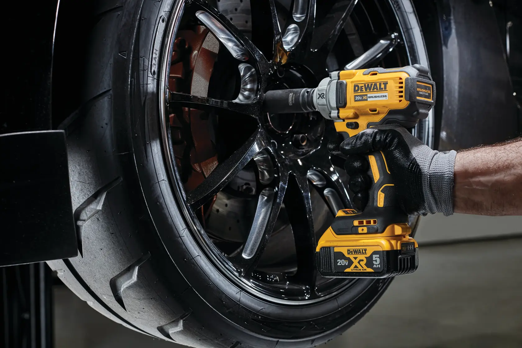 Una persona utiliza una llave de impacto inalámbrica DEWALT para trabajar en las tuercas de una rueda de coche. La herramienta tiene un diseño amarillo y negro y se opera con una mano enguantada.