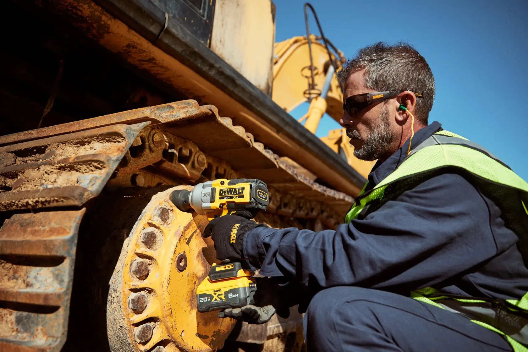 Persona usa herramienta DEWALT en maquinaria pesada al aire libre, con guantes y equipo de seguridad.