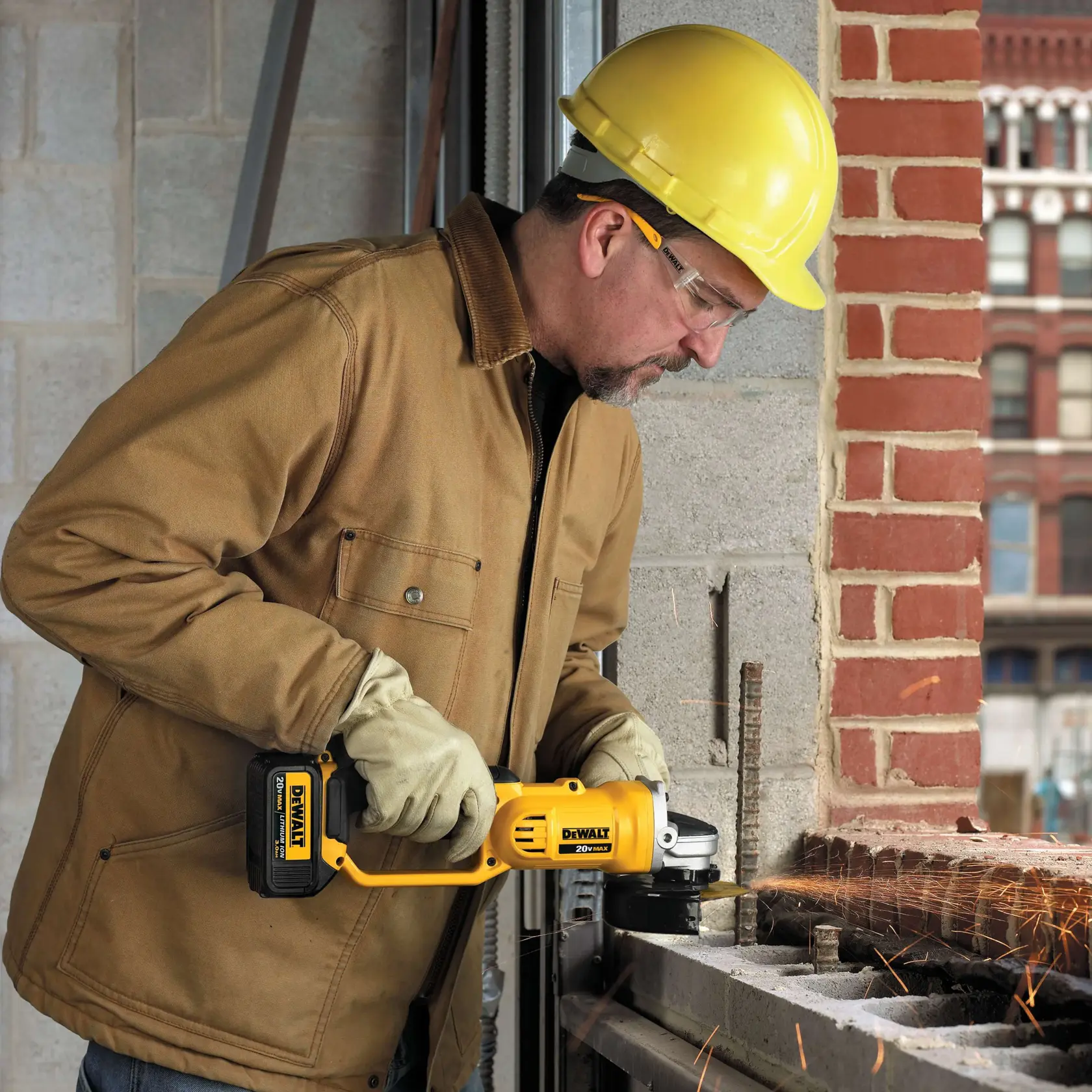 Persona con casco amarillo y chaqueta marrón de trabajo utilizando una amoladora angular inalámbrica DEWALT para cortar varilla metálica, con chispas en un sitio de construcción.