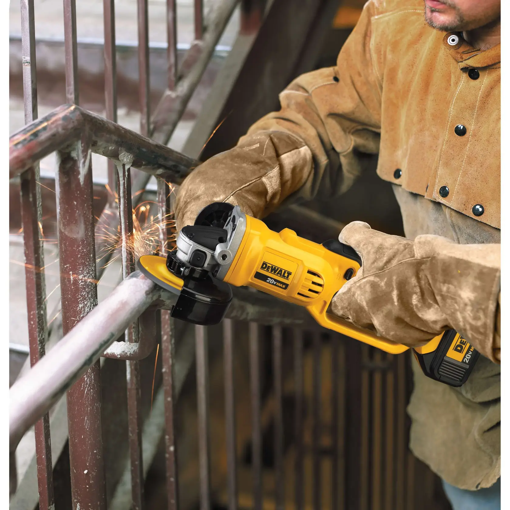 Una persona con guantes protectores y una chaqueta de trabajo marrón utiliza una amoladora angular inalámbrica amarilla DEWALT 20V Max para cortar o pulir un tubo metálico, generando chispas.