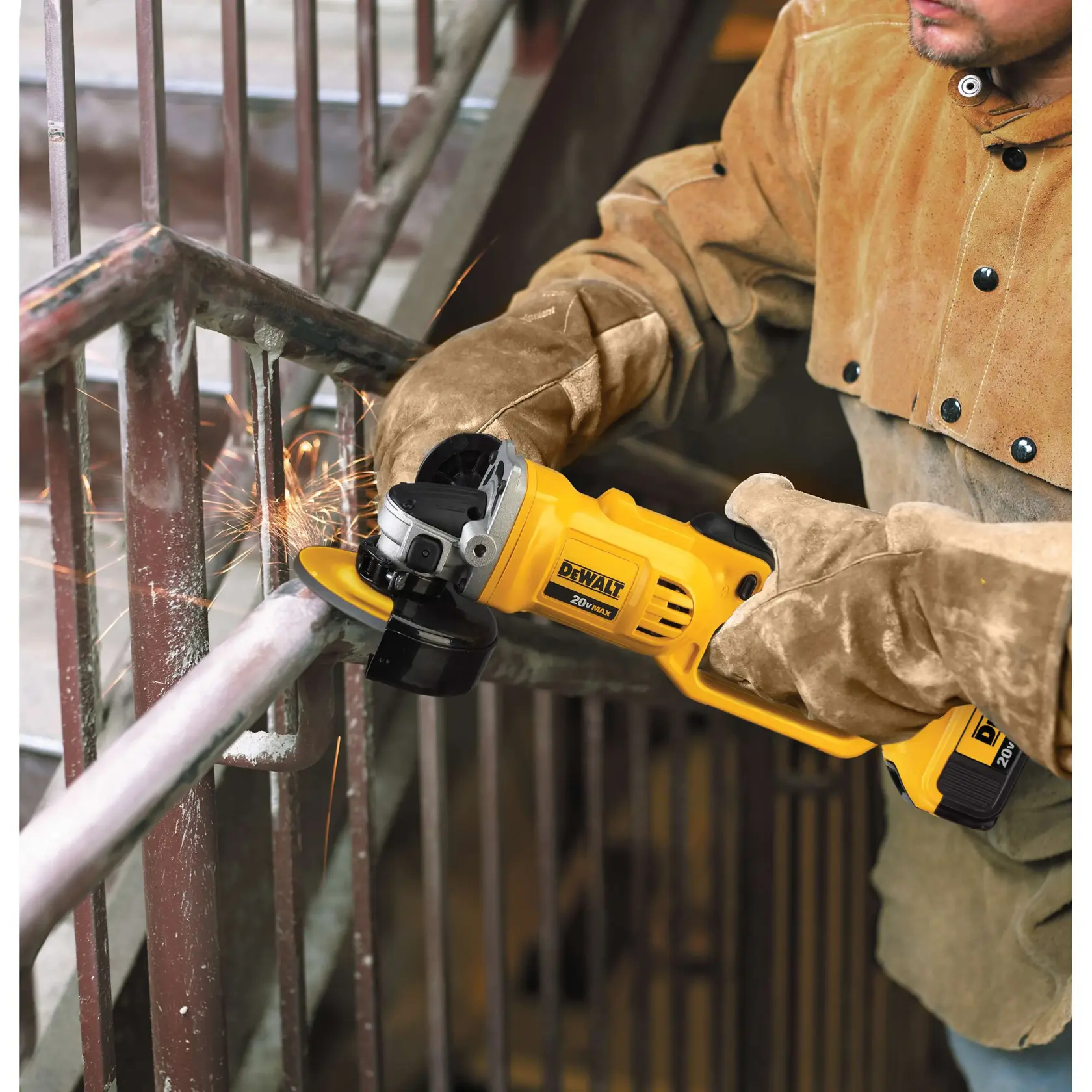 Una persona con guantes y chaqueta protectora utiliza una amoladora angular inalámbrica amarilla DEWALT para cortar una barandilla de metal, generando chispas.