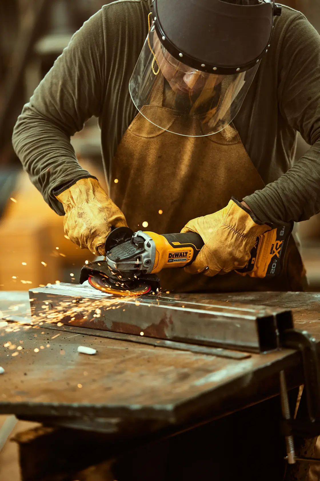 Persona usa amoladora DEWALT DCG413B en metal, con guantes, delantal y protector facial, saltan chispas.
