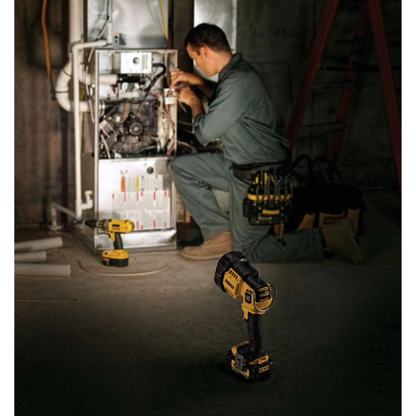 Una persona está de rodillas y trabaja en una caldera en un taller o sótano, con herramientas DEWALT, incluido un foco inalámbrico (DCL043) que aparece en primer plano y otras herramientas DEWALT cerca. El rostro de la persona está borroso para proteger la privacidad.