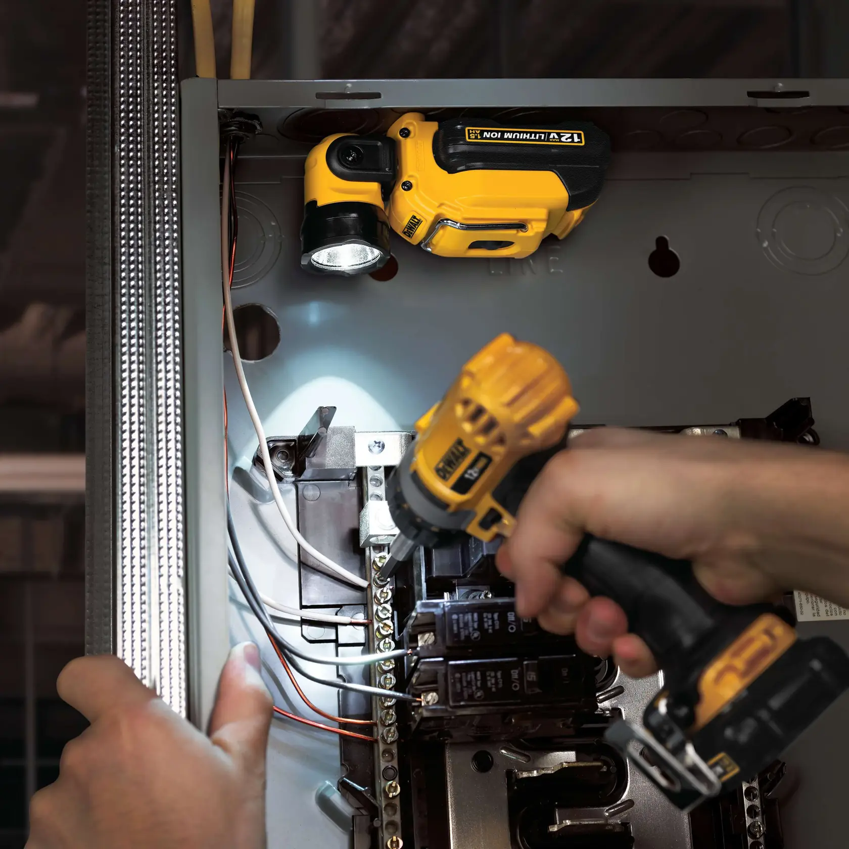 Vista de cerca de una persona utilizando un taladro inalámbrico DEWALT en un panel eléctrico, con una lámpara LED de trabajo DEWALT iluminando la zona.