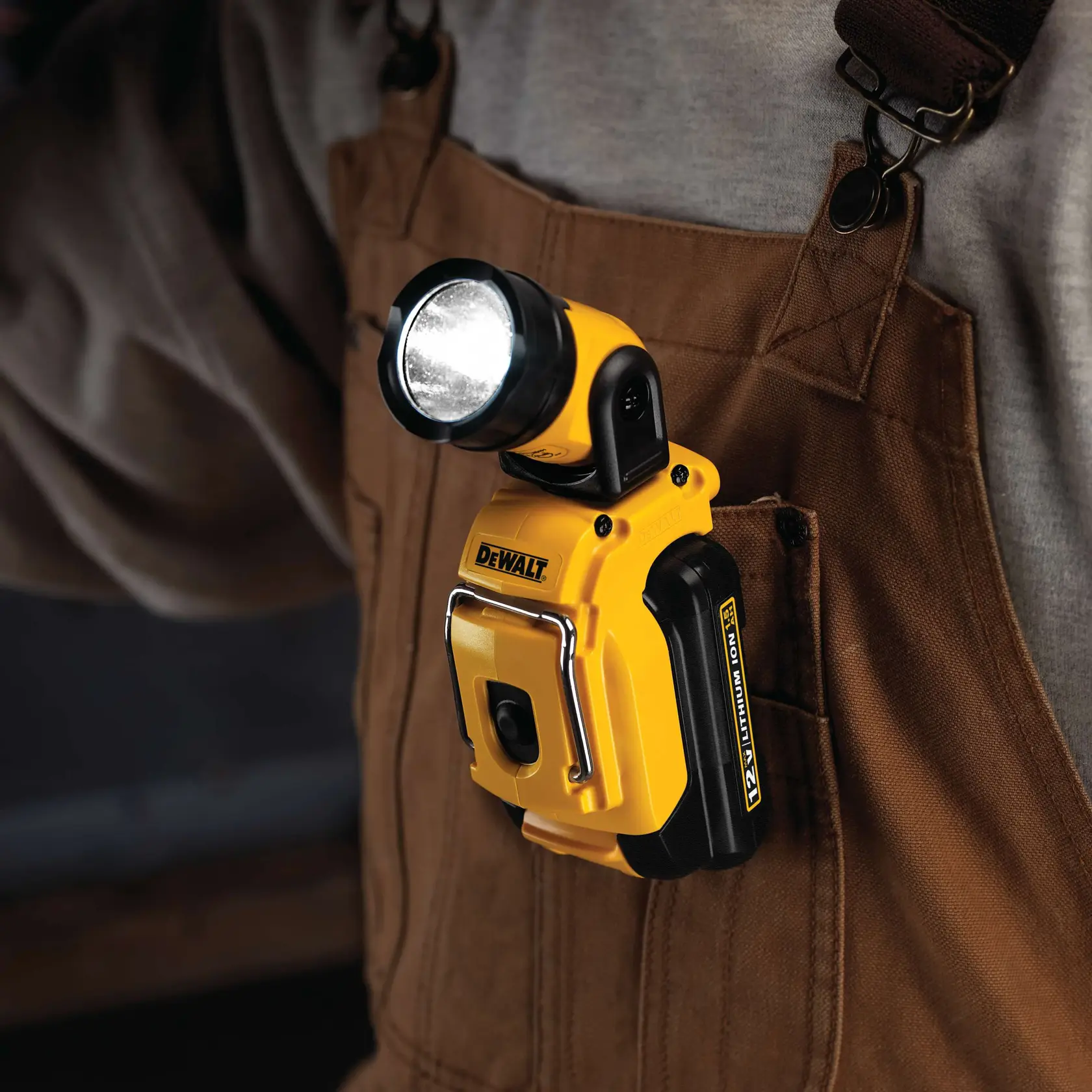 Una luz de trabajo compacta amarilla DEWALT DCL510 sujetada al bolsillo frontal de un overol marrón, encendida y usada por una persona.