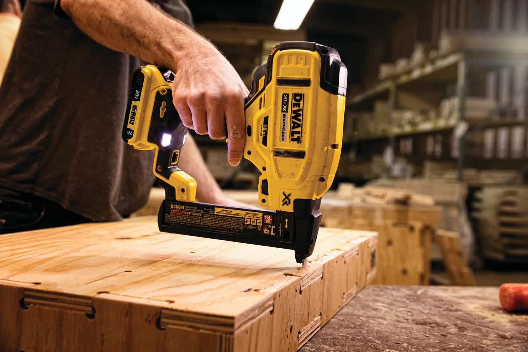 Una persona está usando una clavadora inalámbrica DEWALT DCN681B para fijar tablones de madera en un taller.