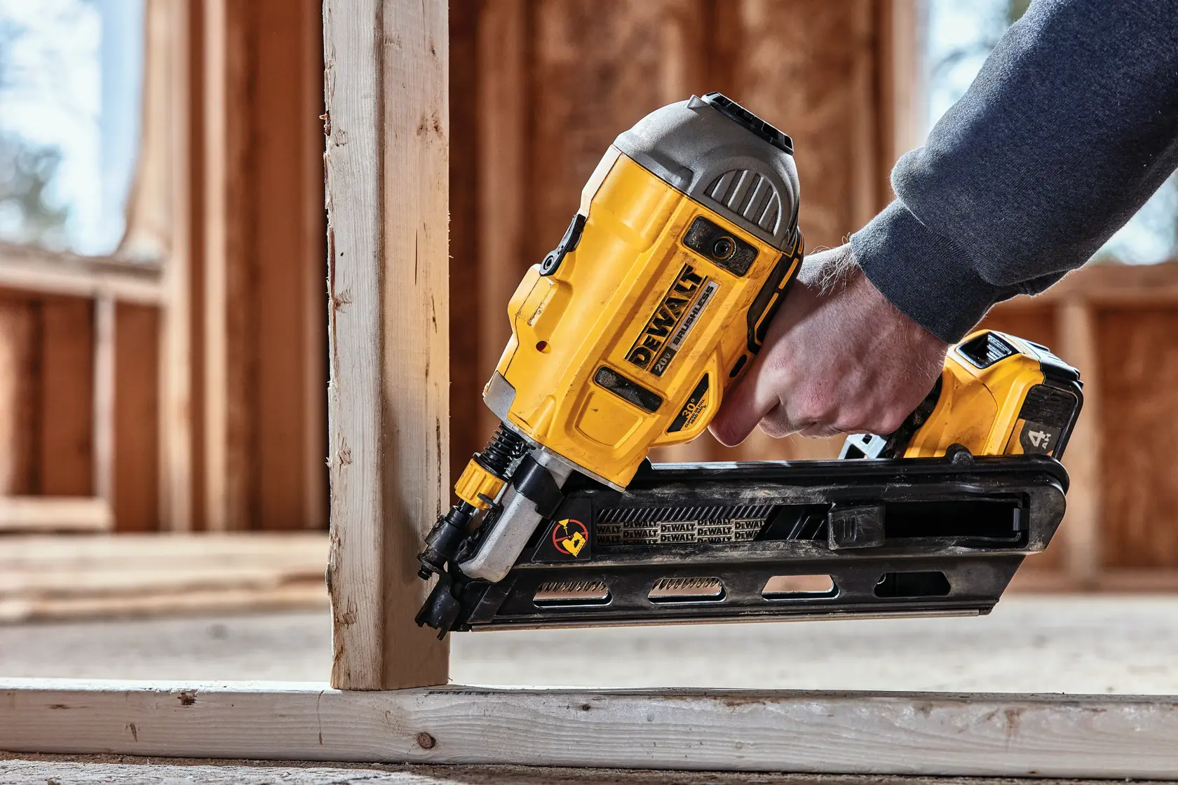 Una persona usa una clavadora inalámbrica DEWALT para fijar una viga de madera en una obra de construcción.