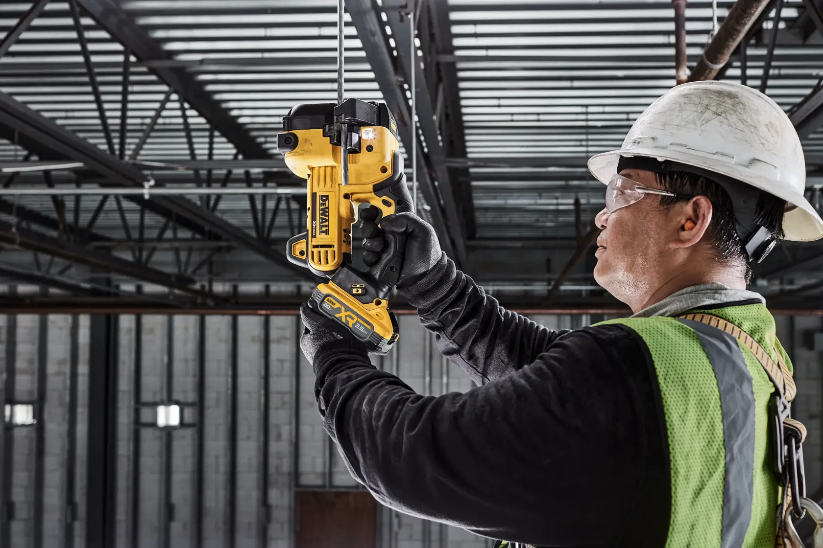 Un trabajador de la construcción con casco y chaleco de seguridad utiliza una herramienta DEWALT DCS350B para cortar una varilla de metal en un entorno industrial.