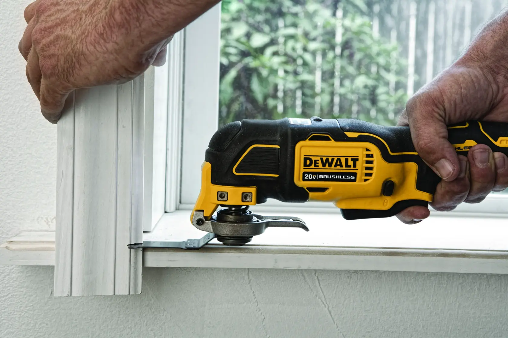 Una herramienta multifunción oscilante DEWALT 20V sin escobillas se utiliza para cortar la parte inferior de un adorno de madera cerca de una ventana.