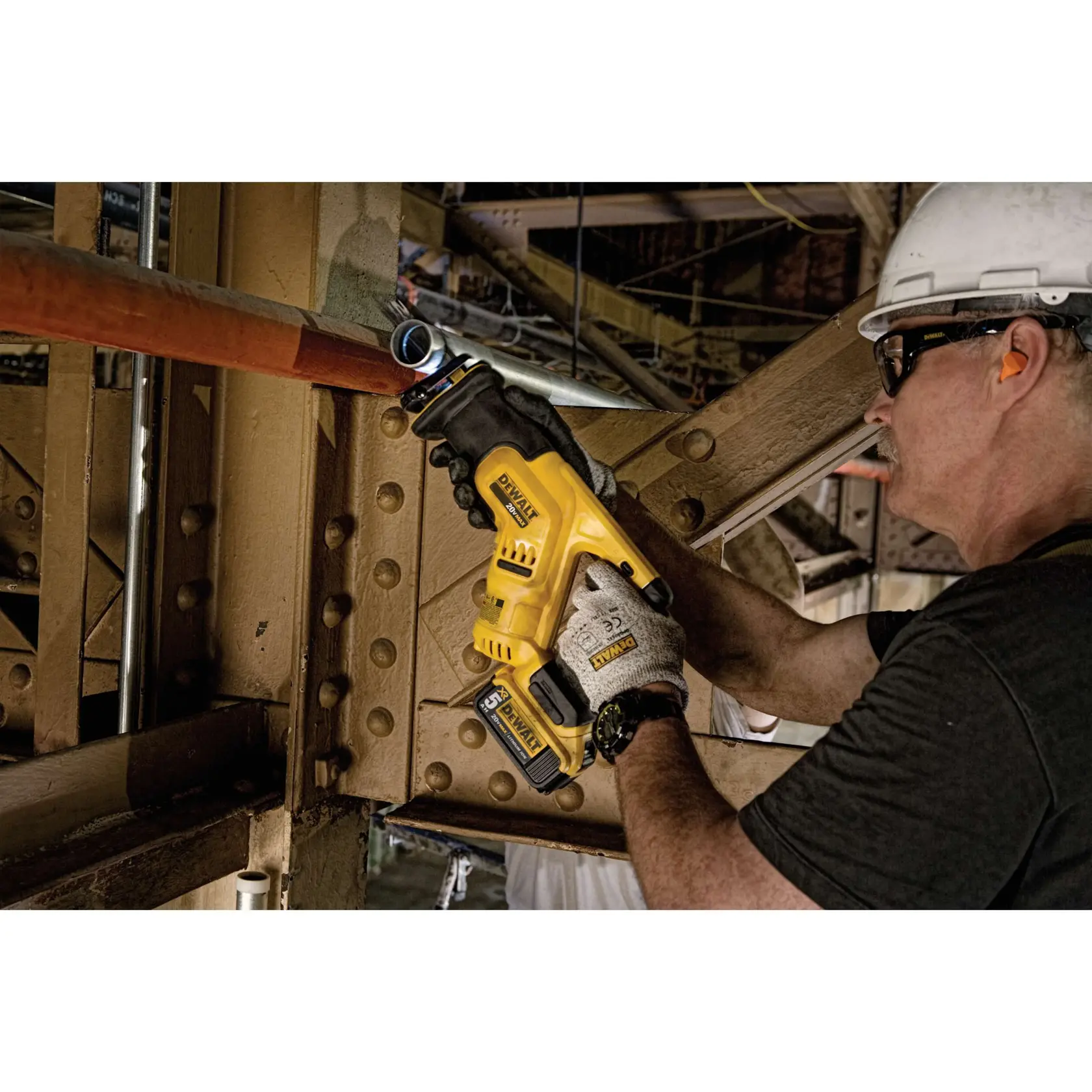Una persona con guantes y casco utiliza una sierra recíproca inalámbrica DEWALT DCS387B para cortar una tubería de metal en un entorno industrial.