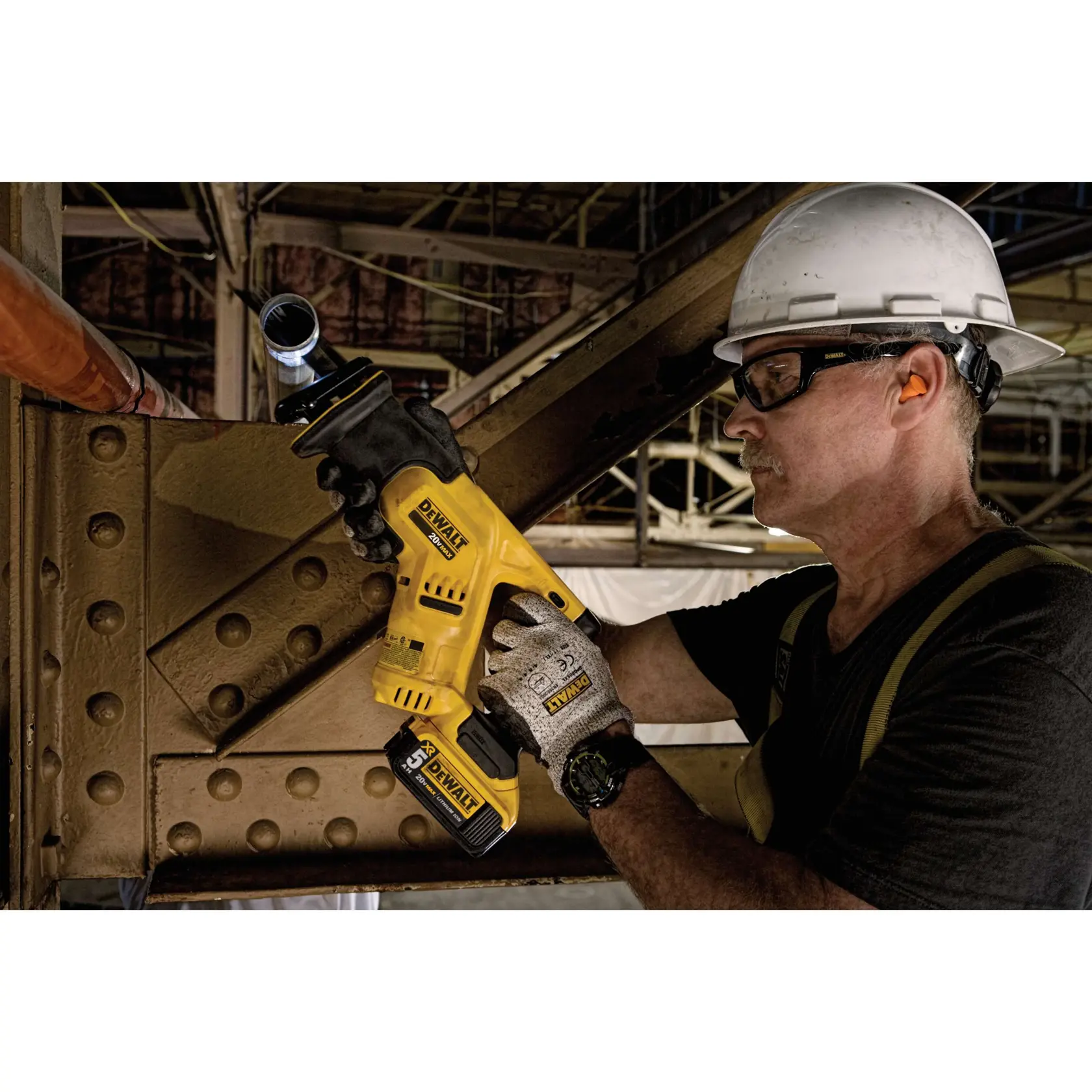 Una persona con casco y guantes está usando una sierra reciproca amarilla DEWALT inalámbrica para cortar una tubería de metal en un sitio de construcción industrial. El rostro de la persona está difuminado para preservar la privacidad.