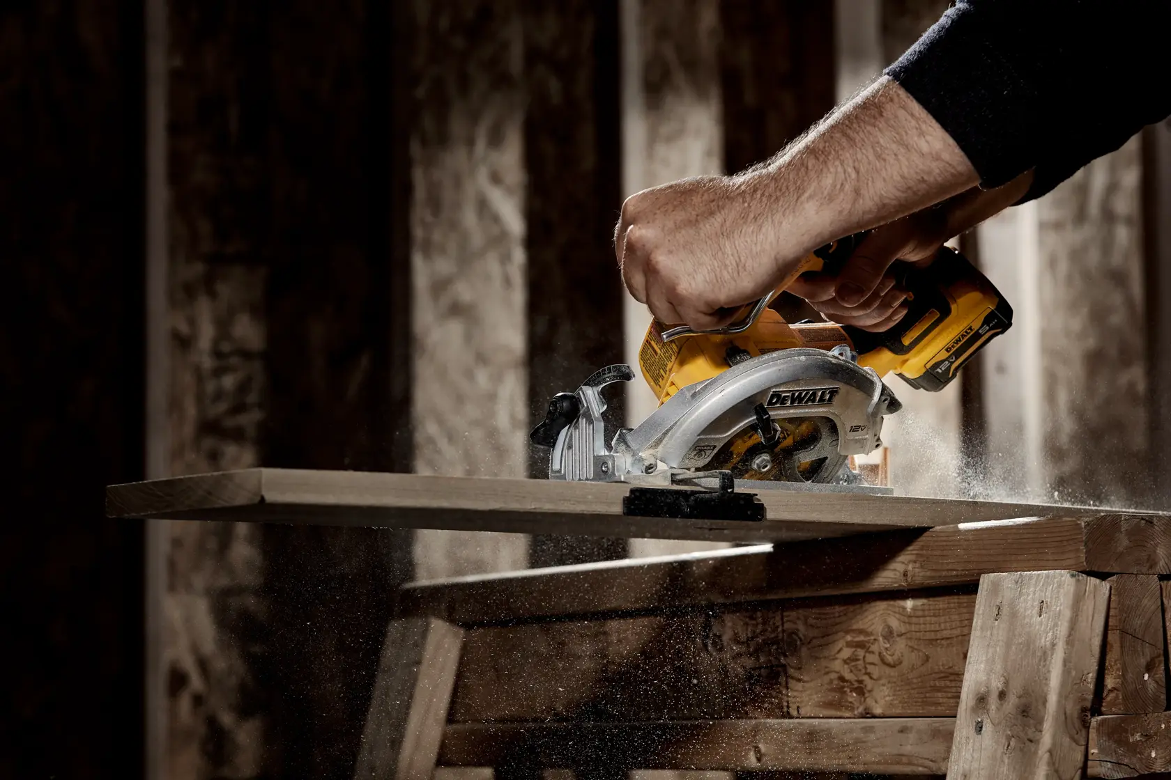 Una persona utiliza una sierra circular inalámbrica DEWALT para cortar una tabla de madera, con aserrín volando en un taller.