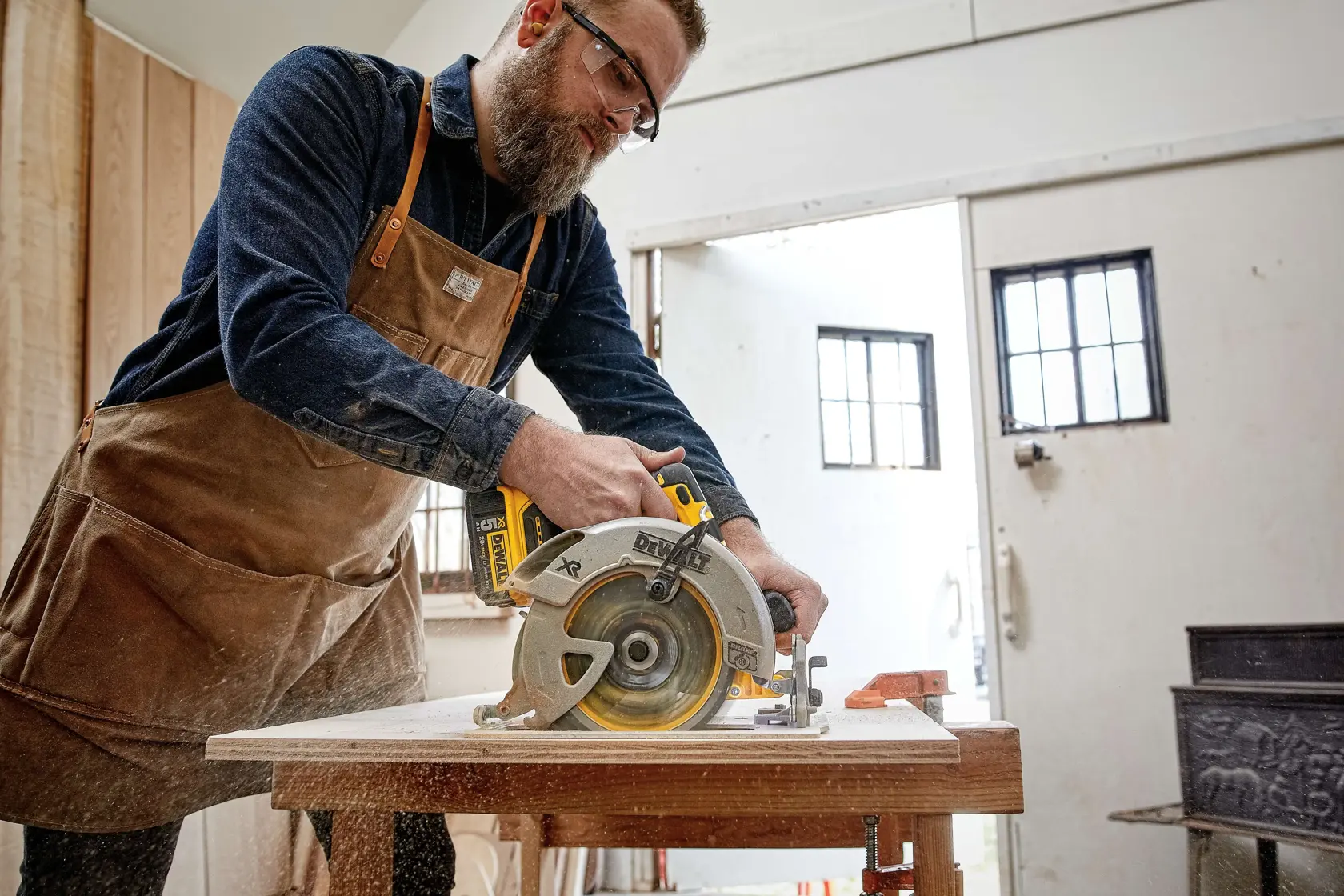 Persona usando una sierra circular DEWALT DCS570B para cortar madera en un banco de taller.