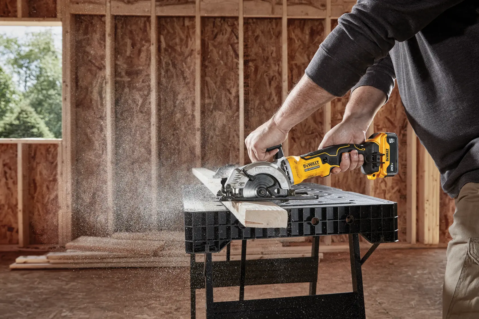 Una persona utiliza una sierra circular inalámbrica DEWALT DCS571B para cortar una pieza de madera en un banco de trabajo en un sitio de construcción.