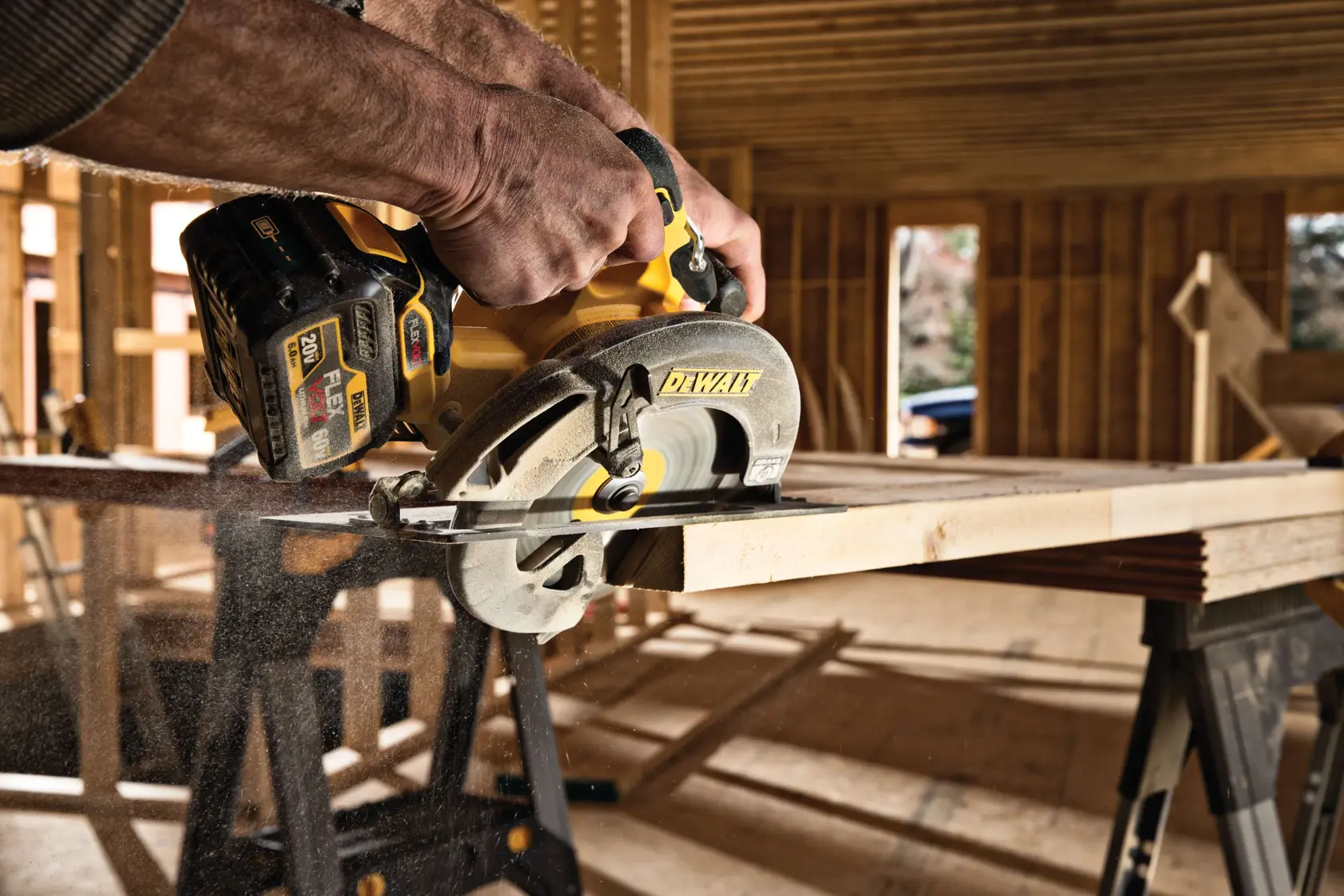 Vista de primer plano de una sierra circular inalámbrica DEWALT en uso, cortando una tabla de madera dentro de una obra en construcción con estructura de madera sin terminar.