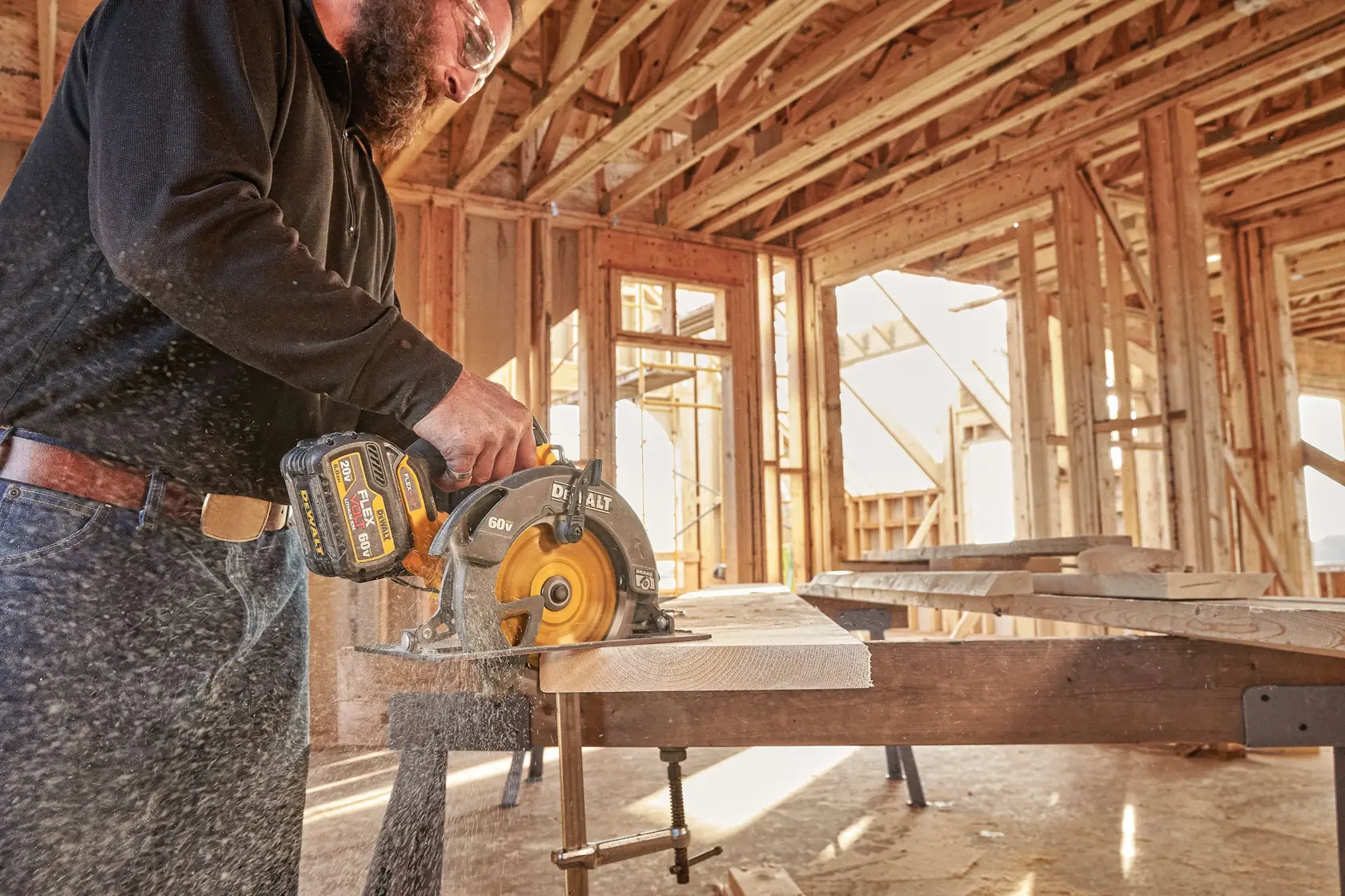 Una persona utiliza una sierra circular inalámbrica DEWALT de 60V (modelo DCS575T2) para cortar una tabla de madera en un espacio de construcción sin terminar con estructura de madera expuesta.