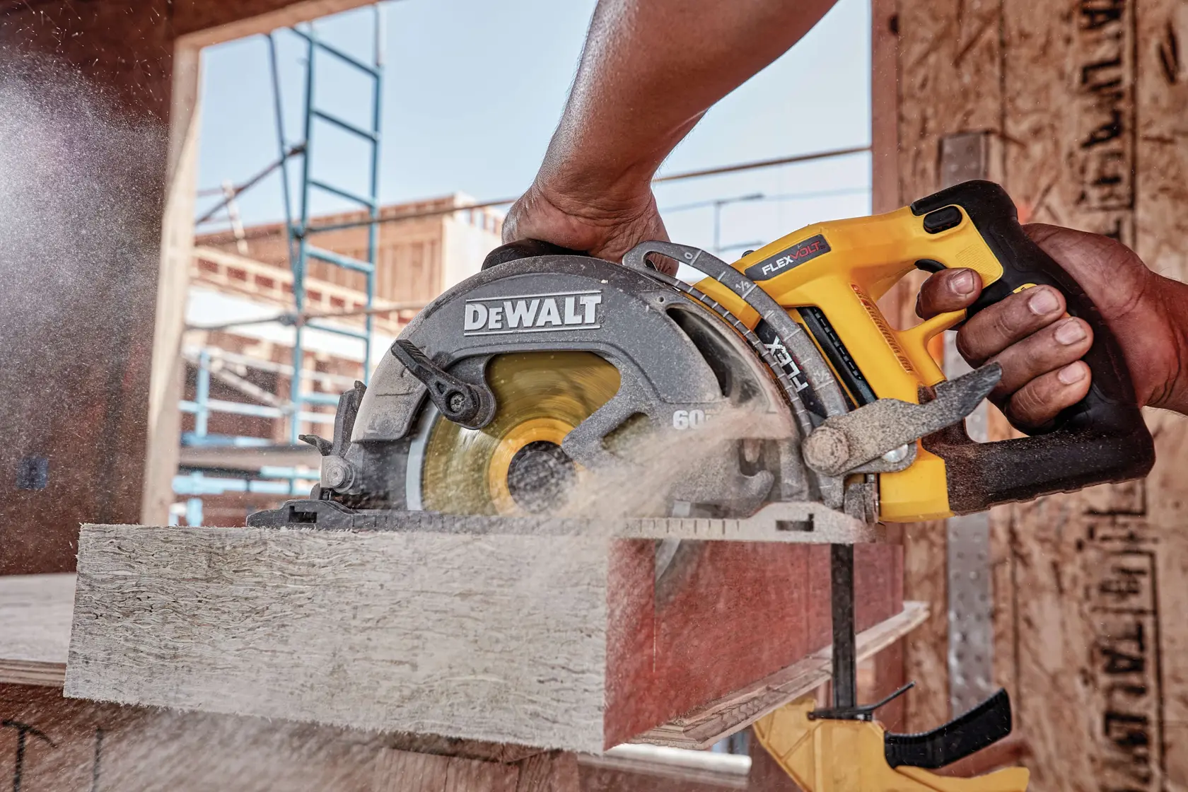 Una persona usa una sierra circular inalámbrica DEWALT para cortar un trozo de madera en una obra, con aserrín volando por el aire.