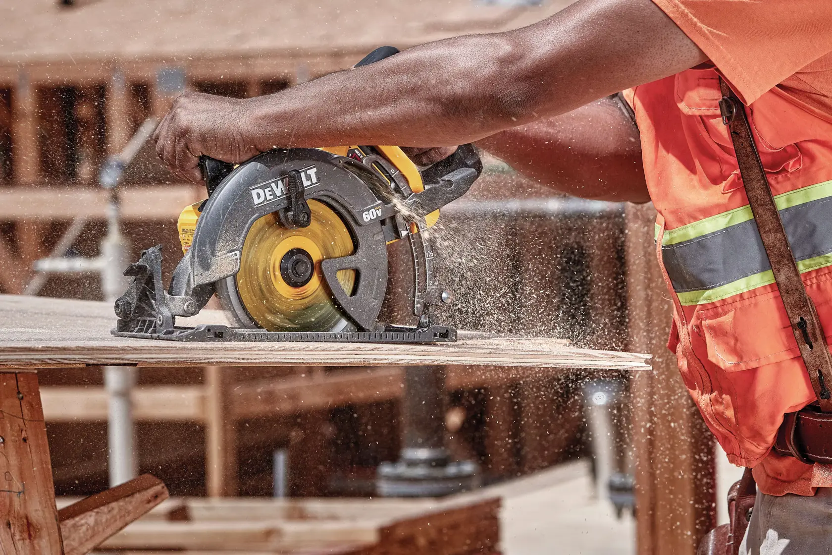 Una persona con un chaleco de seguridad naranja está usando una sierra circular DEWALT DCS577B para cortar una tabla de madera en un sitio de construcción. El aserrín es visible en el aire.