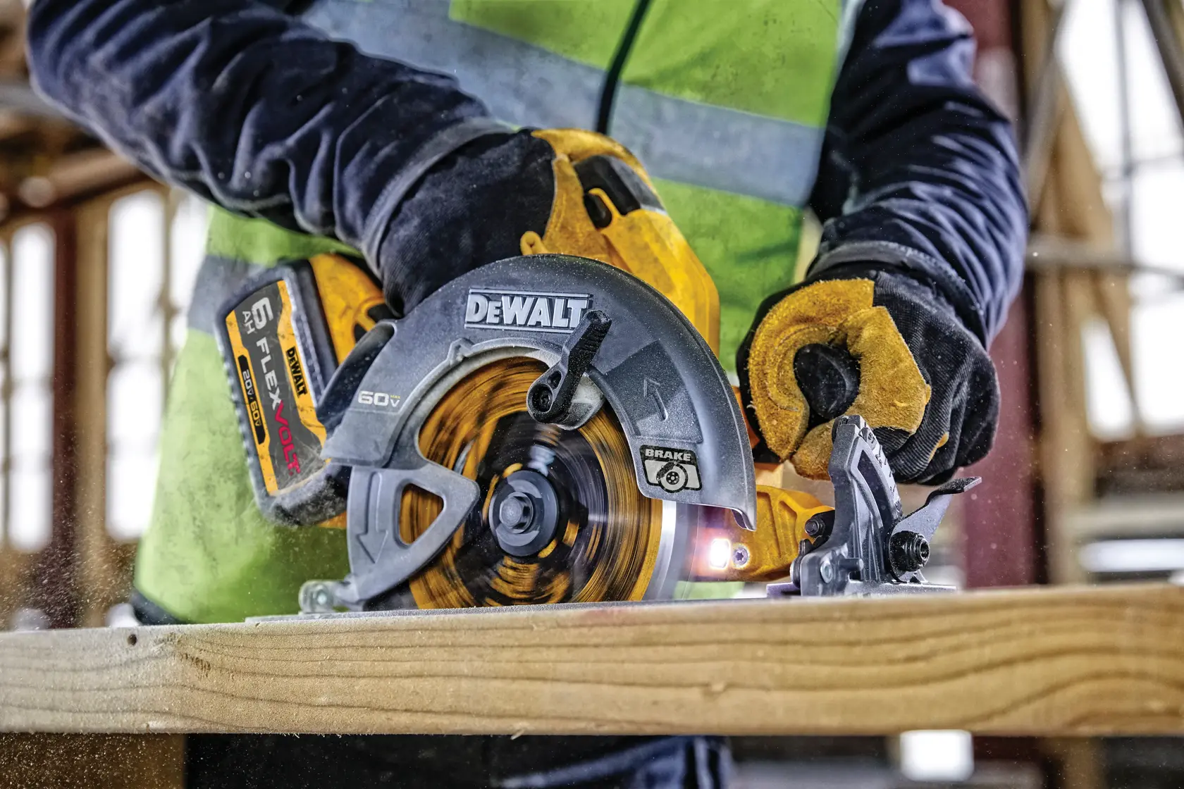 Una persona con guantes y chaleco de alta visibilidad utiliza una sierra circular DEWALT DCS578B para cortar una tabla de madera en una obra de construcción.