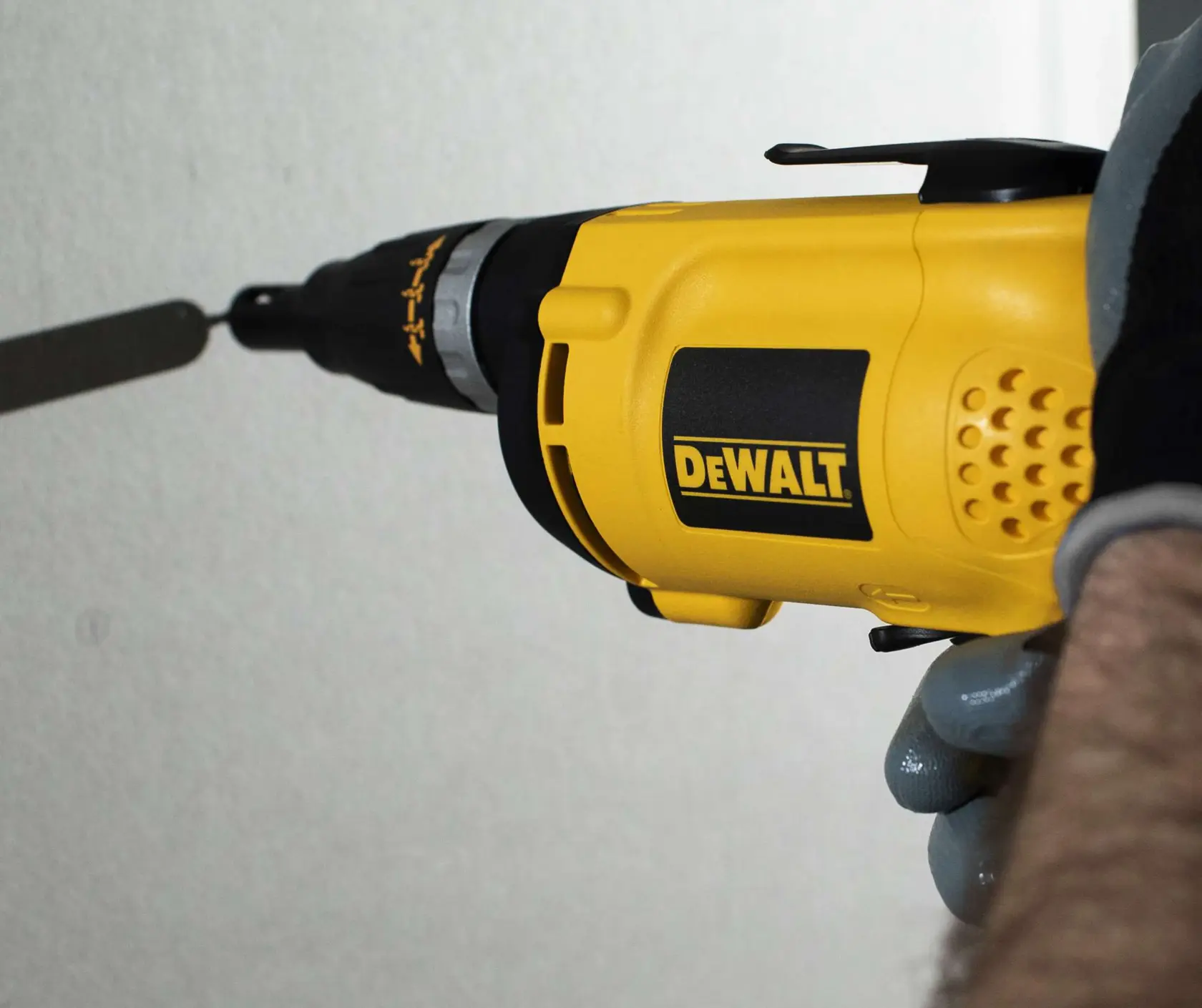 Vista en primer plano de una persona utilizando un destornillador eléctrico amarillo DEWALT (modelo DW255) para atornillar en una pared.