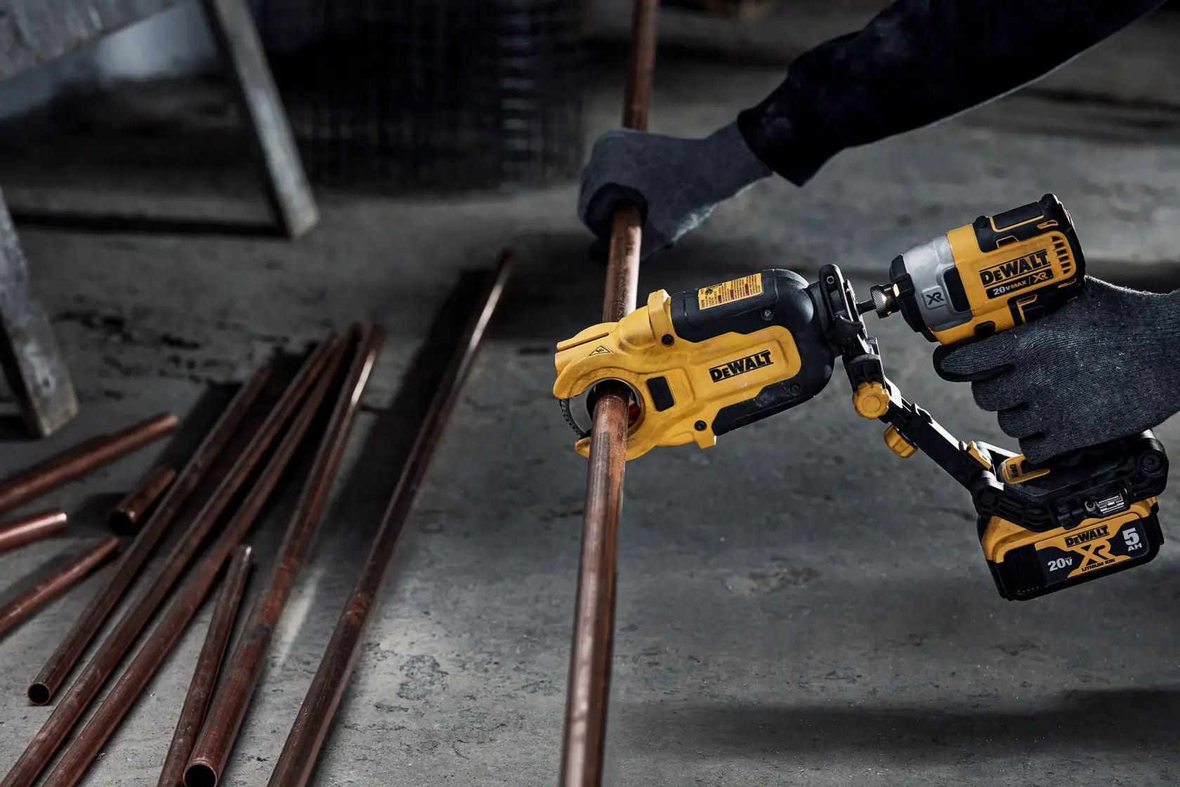 Una persona con guantes utiliza una herramienta eléctrica DEWALT para cortar un tubo de cobre. Varios tubos de cobre están en el suelo cerca.