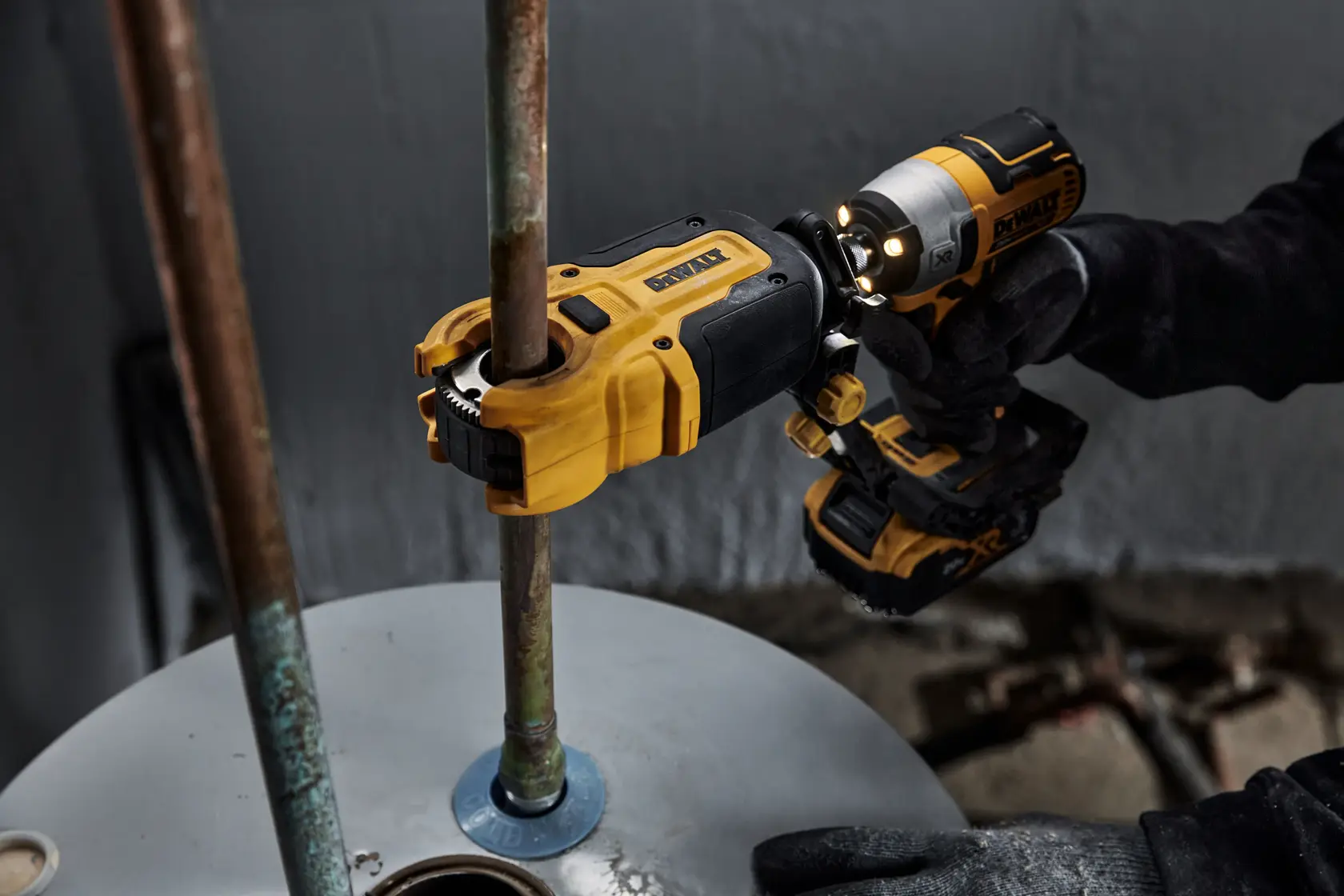 Una herramienta eléctrica DEWALT se utiliza para cortar o trabajar en una tubería de metal fijada a una superficie. El trabajador lleva guantes negros mientras opera la herramienta amarilla y negra.