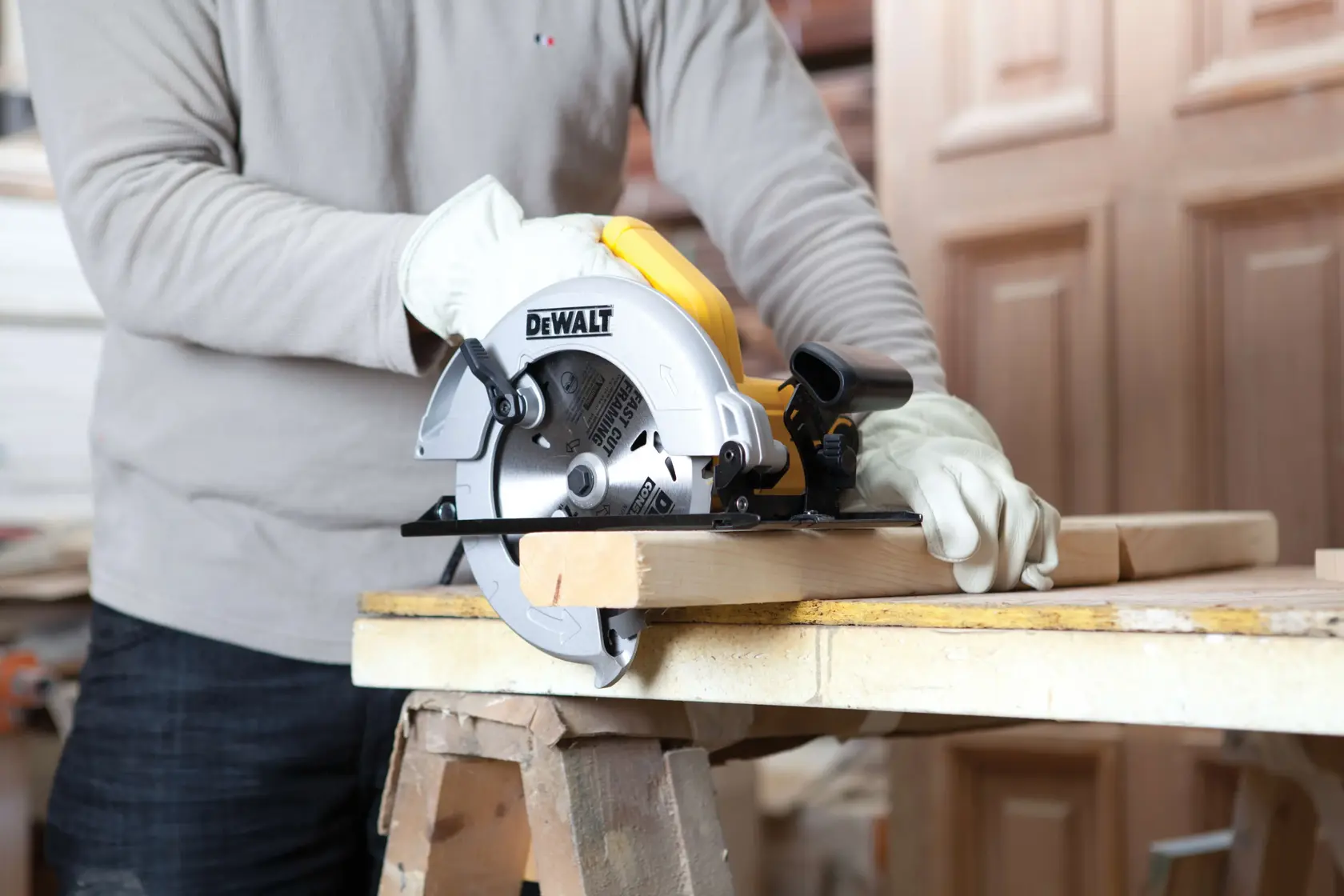 Una persona con guantes está usando una sierra circular DEWALT (modelo DWE560) para cortar una tabla de madera en un banco de trabajo.