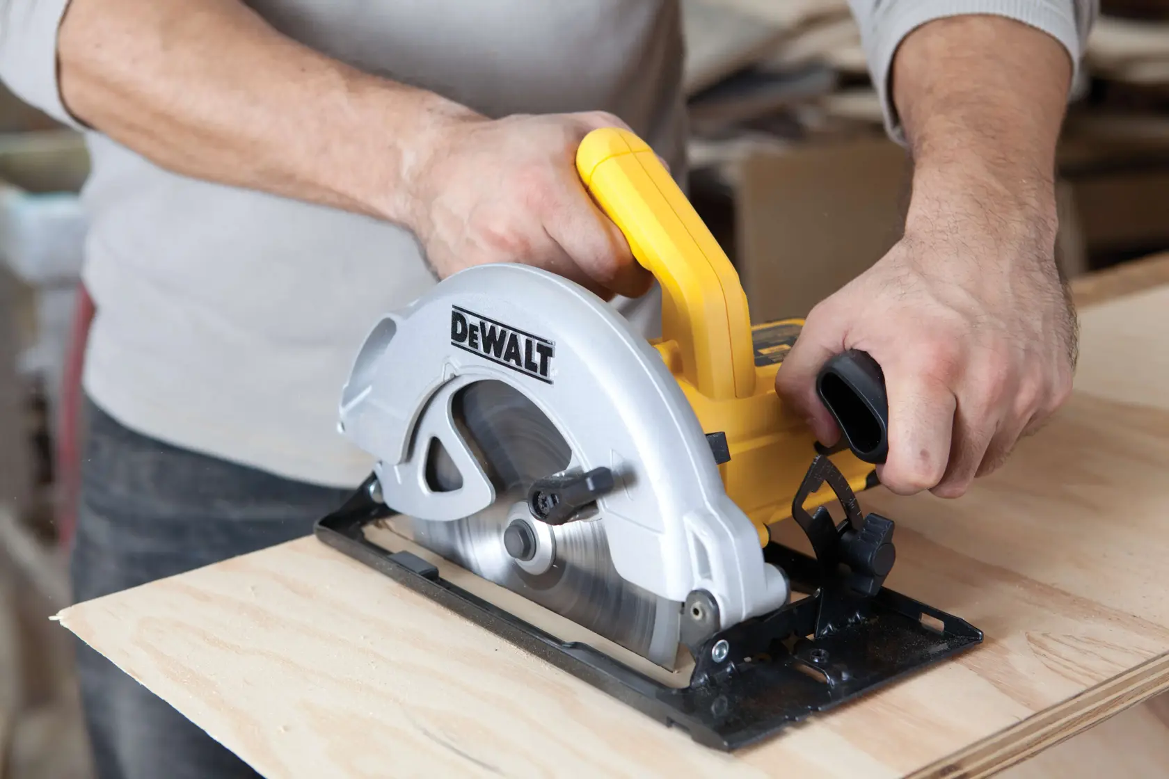 Una persona utiliza una sierra circular DEWALT DWE560 para cortar un trozo de madera. La herramienta tiene un mango amarillo y una carcasa plateada para la hoja.