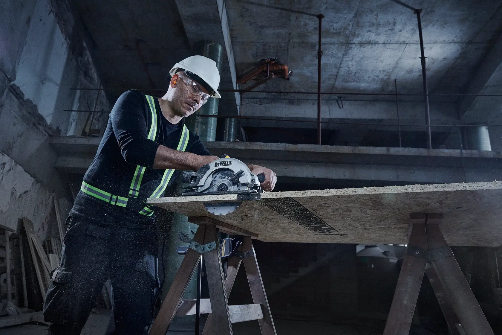 Una persona con casco de seguridad y chaleco reflectante utiliza una sierra circular DEWALT para cortar una tabla de madera apoyada en dos caballetes en un entorno de construcción.