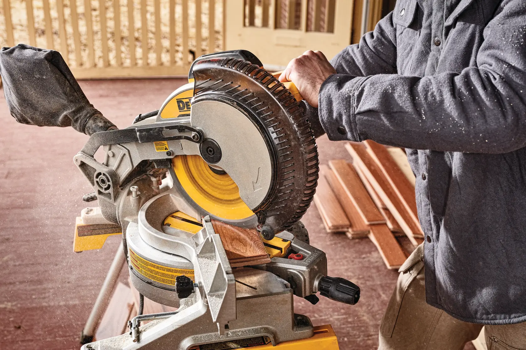 Una persona utilizando una sierra de inglete Dewalt DWS713 para cortar una pieza de madera, con la sierra colocada sobre un banco de trabajo y varias piezas de madera en el fondo.
