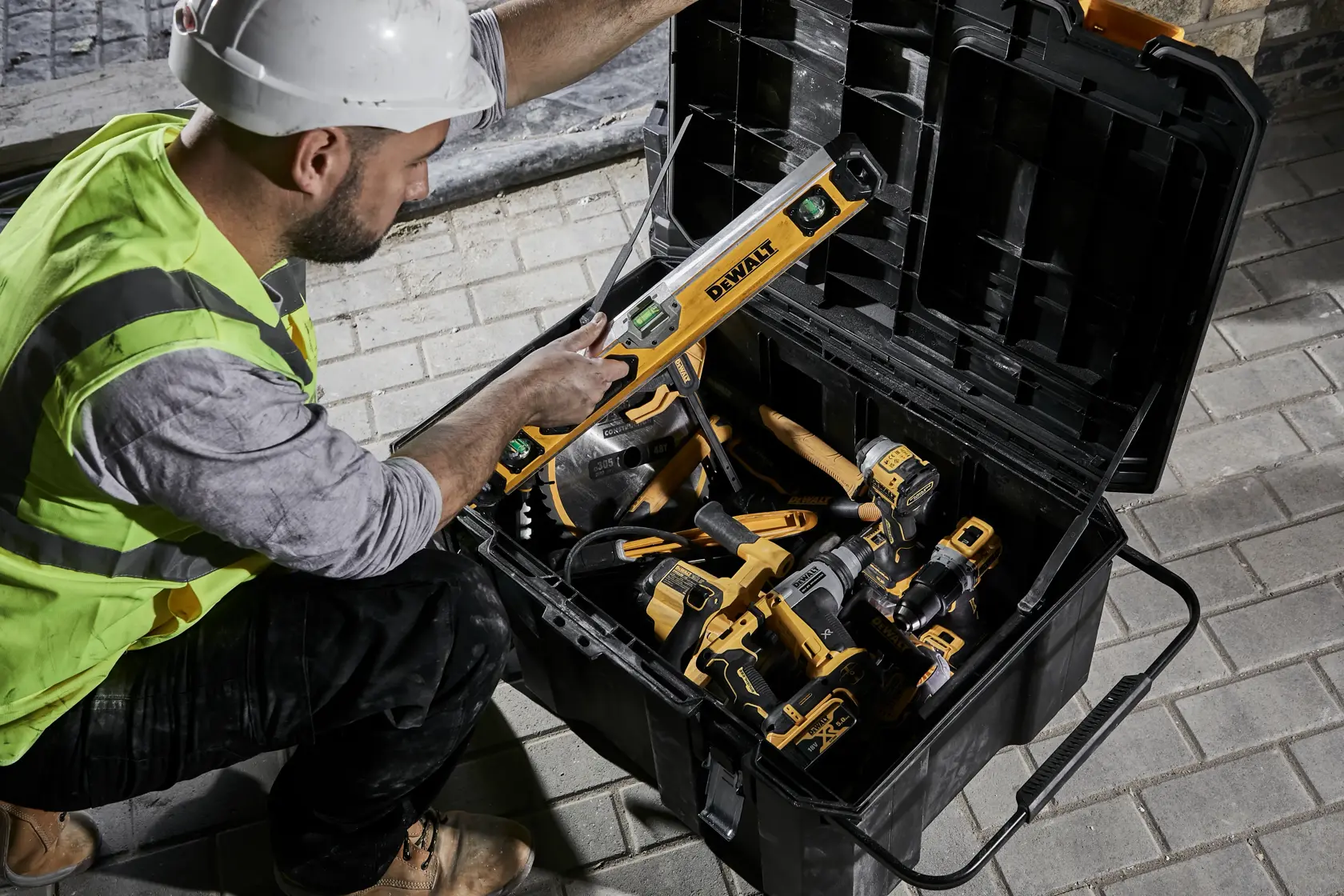 Persona con equipo de seguridad toma herramienta DEWALT de una caja llena de herramientas DEWALT amarillas y negras.