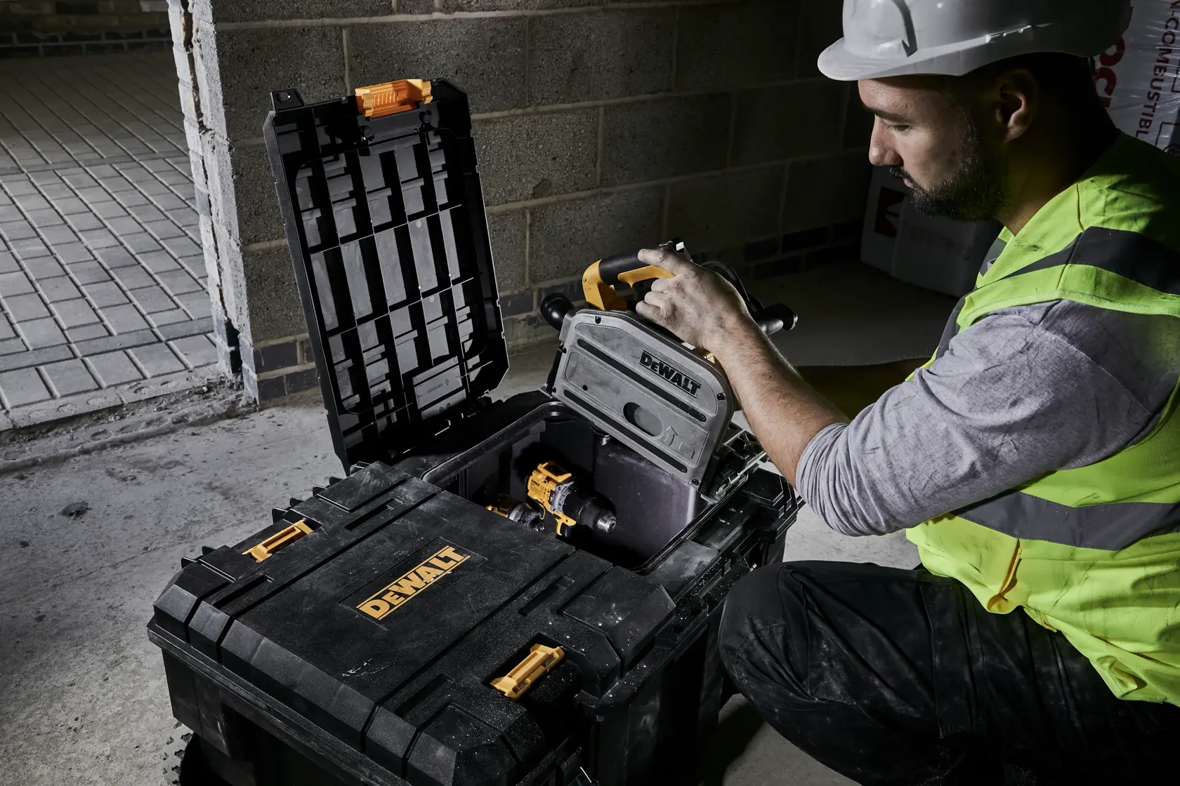 Trabajador abre caja DEWALT con herramientas eléctricas en obra con pared de hormigón.
